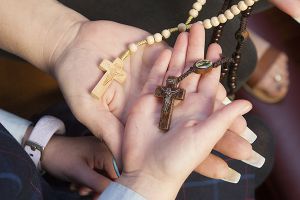 two hands with beige and brown rosary